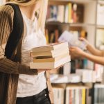 Nahaufnahme eines Bücherstapels, den ein junges High-School-Mädchen in der Bibliothek hält.